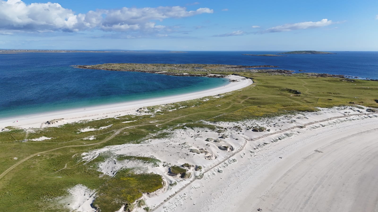Aerial view of a white-sand strand and dunes beside turquoise sea